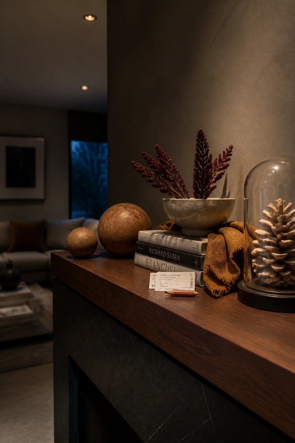 Wooden mantel with stacked books, spheres, dried-flower bowl, and glass-domed pinecone