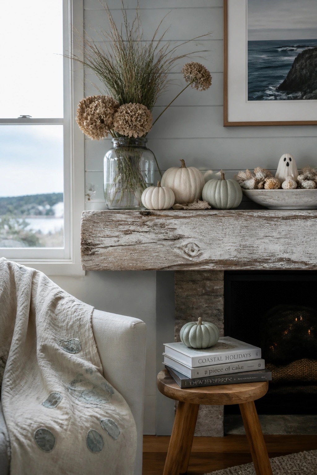 A whitewashed wooden mantel above a fireplace holds several white and pale green pumpkins, a glass jar filled with dried beige flowers, and a small white ghost decoration in a bowl.