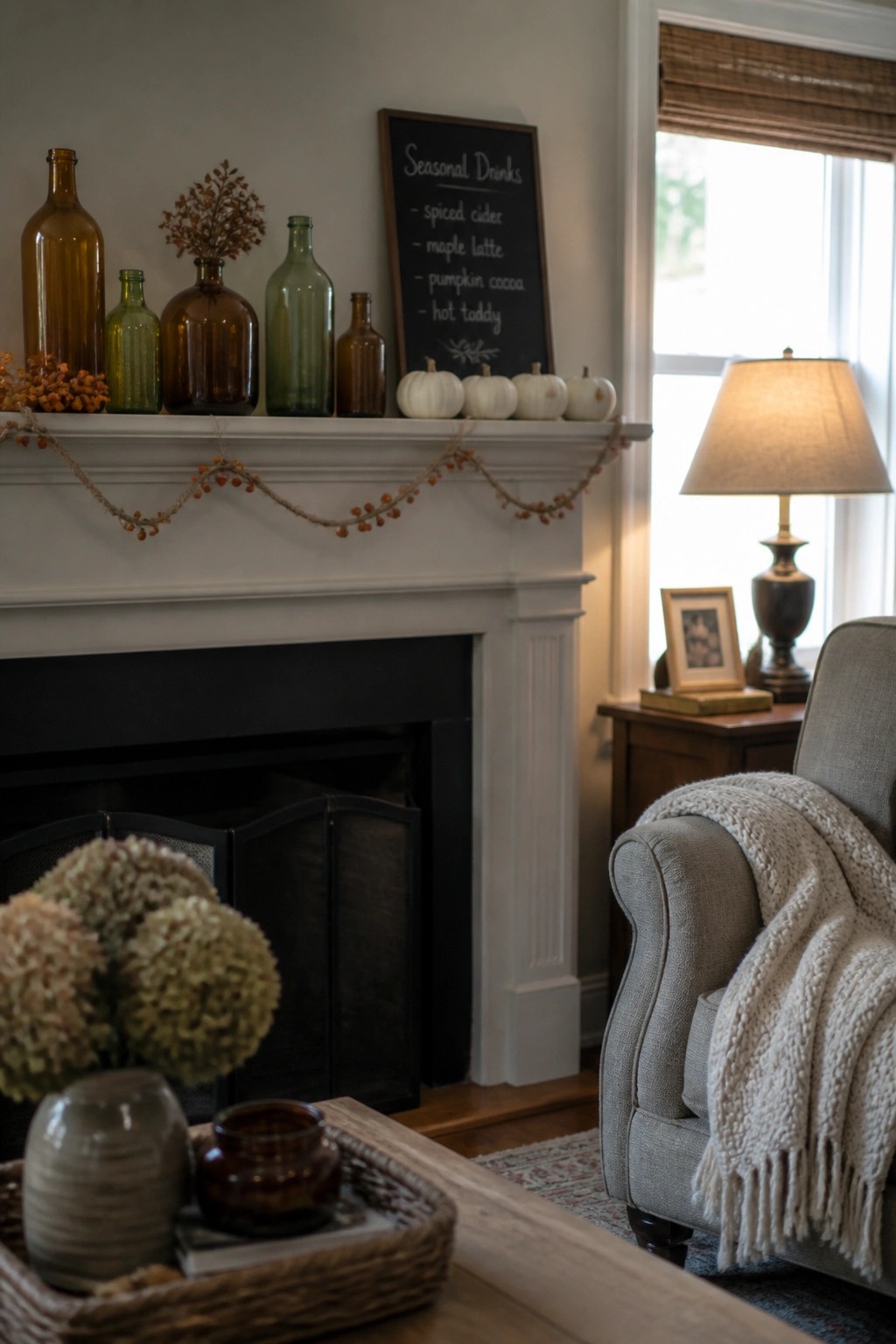 A white fireplace mantel arranged with assorted brown and green glass bottles, small white pumpkins, a berry garland, and a chalkboard sign.