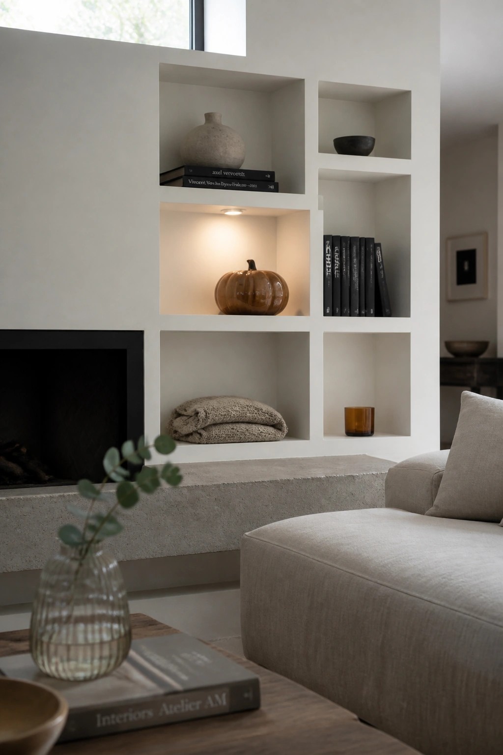 Built-in white shelves around a black fireplace hold books, a ceramic pumpkin, folded blankets, and small decorative objects in a living room setting.