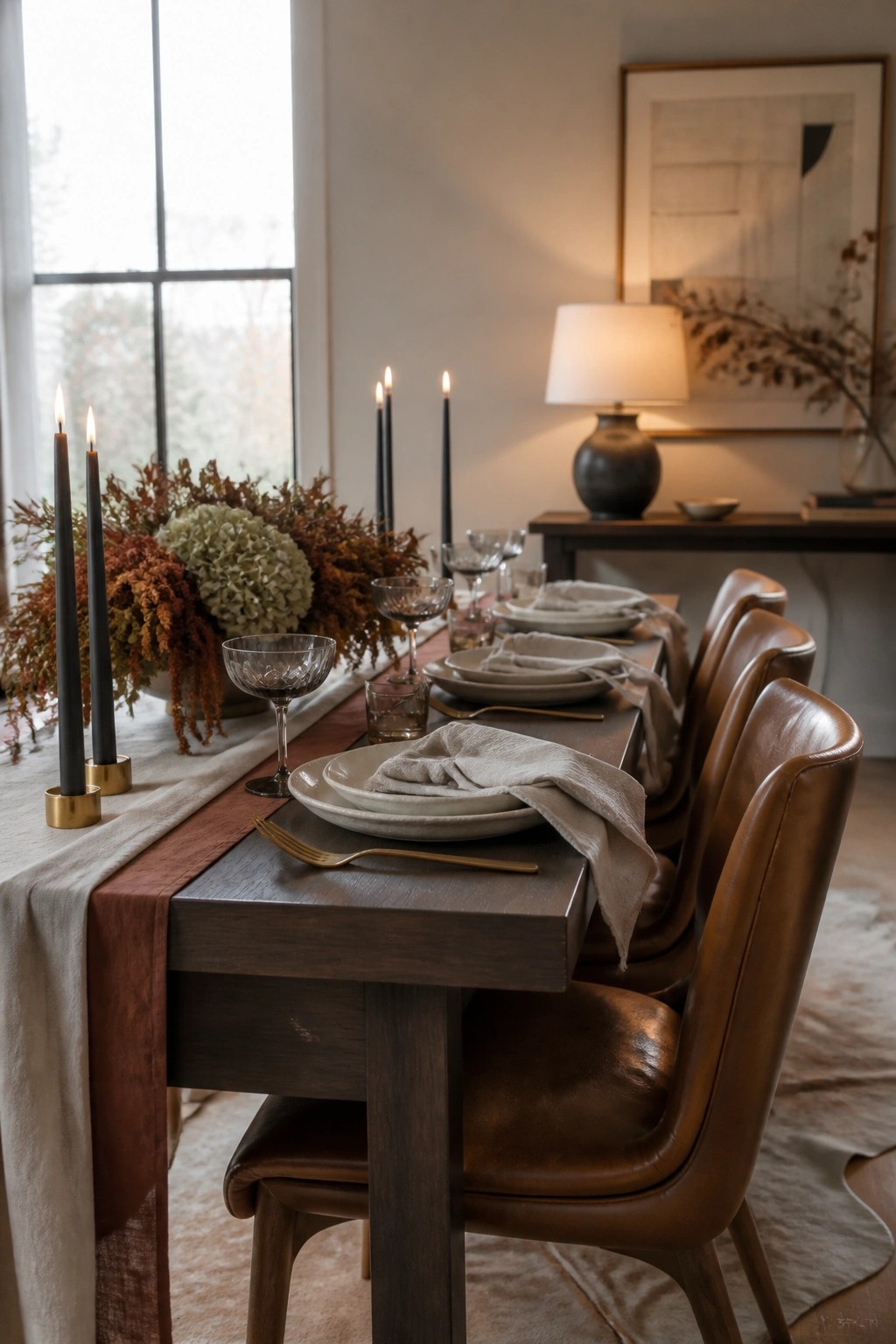 Elegant autumn table setting with leather chairs, black candles, and floral centerpiece.