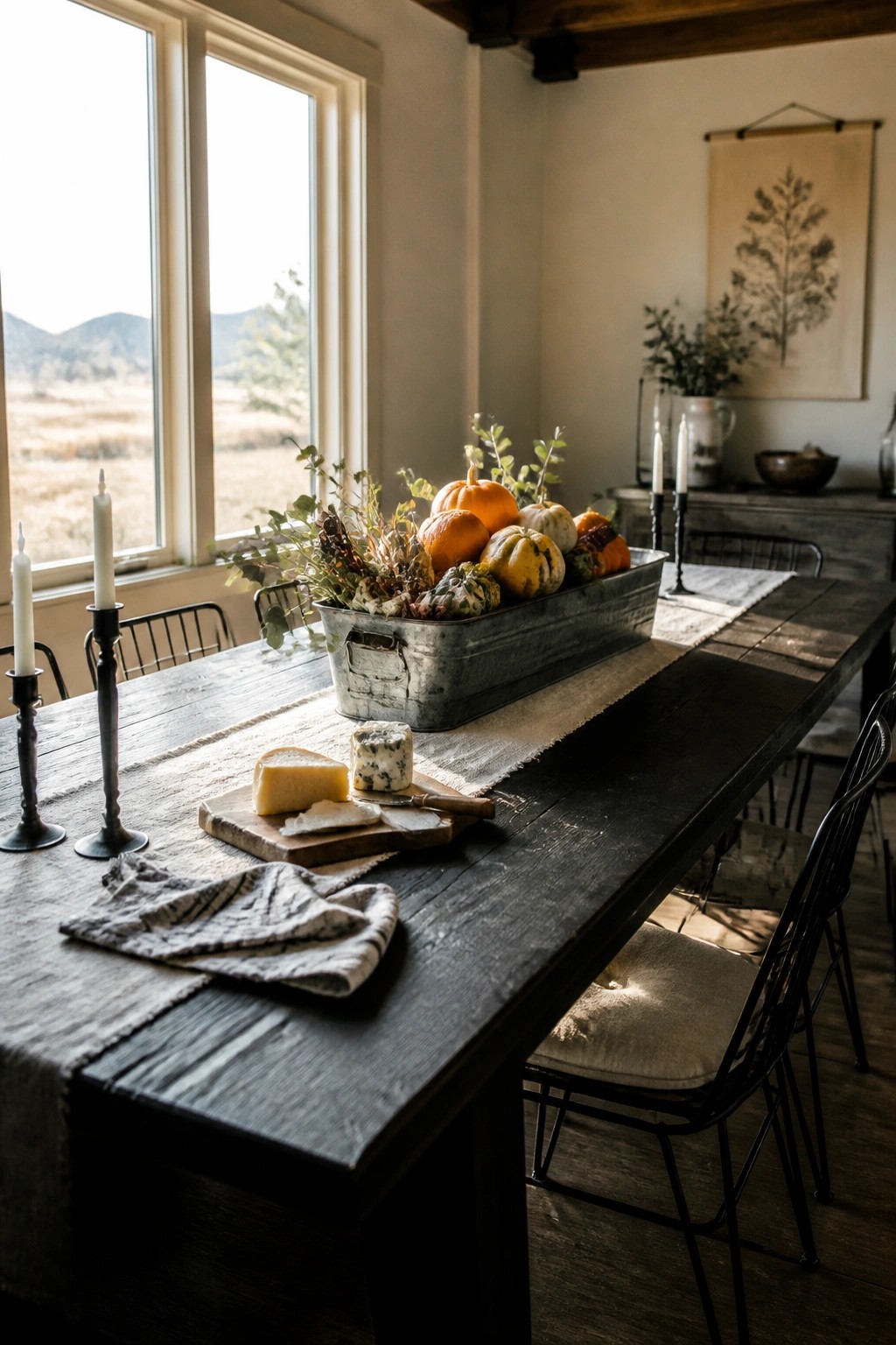 A rustic wooden dining table featuring a long galvanized metal trough filled with pumpkins, gourds, and autumn foliage as a centerpiece.