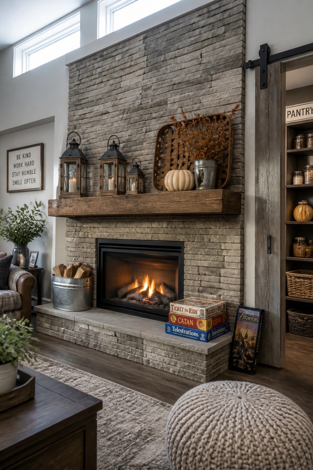 A stacked stone fireplace with a thick wooden mantel holding three lanterns, a wooden tray with dried flowers and a pumpkin, and board games stacked on the hearth.