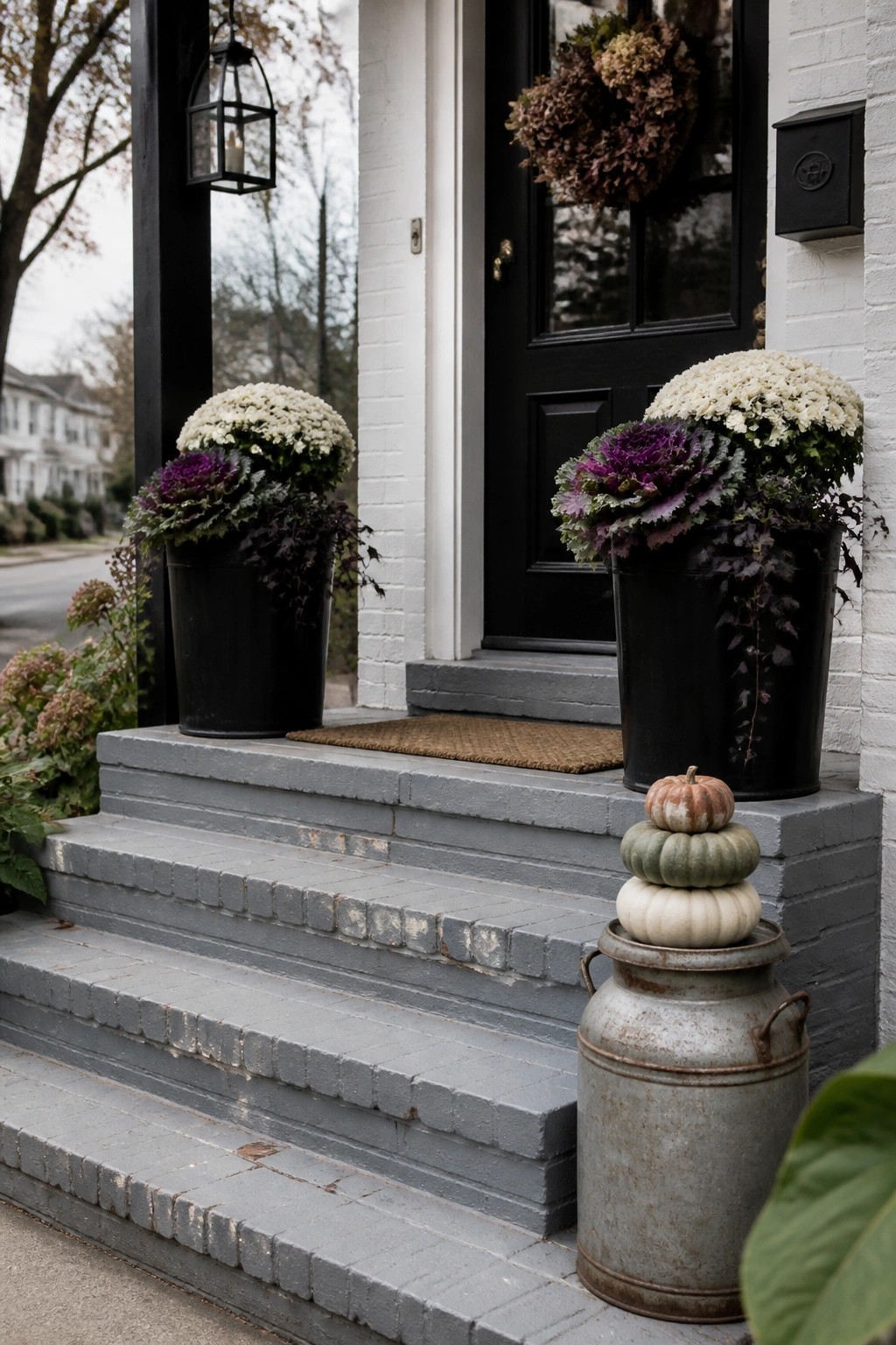 Gray porch steps with black pots of flowers and stacked pumpkins beside black door