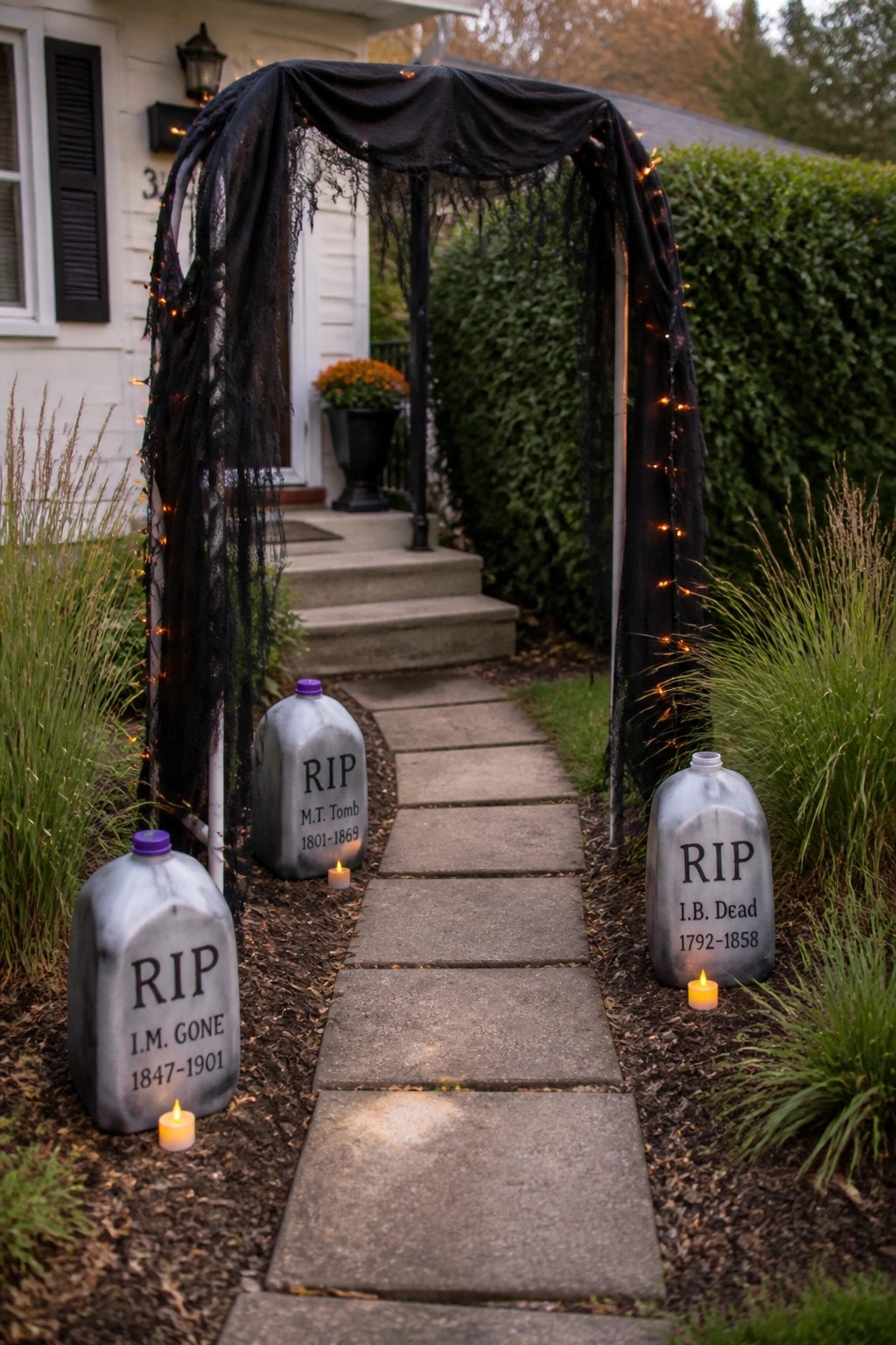 Halloween pathway with black lighted arch, glowing candles, and three RIP tombstones.