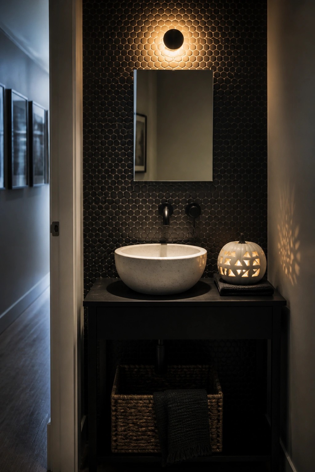 A bathroom with dark hexagonal wall tiles, a white stone vessel sink on a black vanity, and a carved white pumpkin glowing from within on the counter.