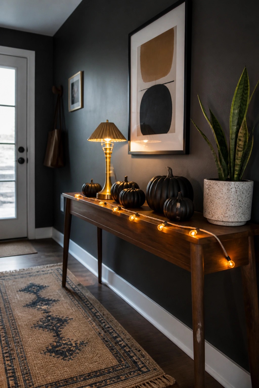 Dark hallway console with black pumpkins, glowing lamp, string lights, and potted plant